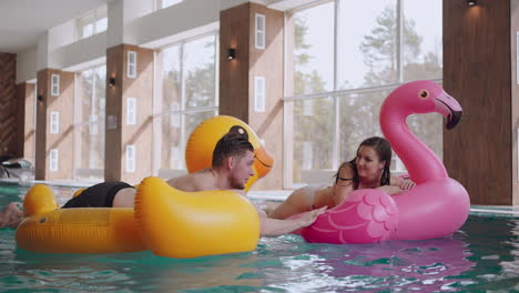 relax-in-thermal-bath-or-wellness-center-man-and-woman-are-swimming-on-funny-inflatable-cirlces